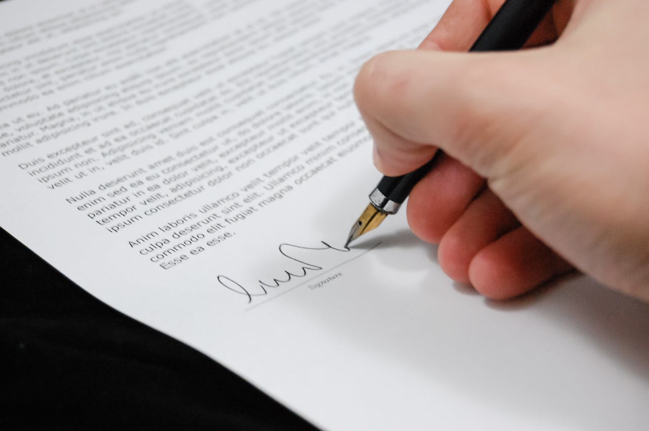 services-02 Close-up of a hand signing a legal document with a fountain pen, symbolizing signature and agreement.